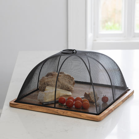Wooden based serving platter with lip that the black mesh metal top sits in to create a protected food cover. Displayed with cheese and cherry tomatoes on a worktop