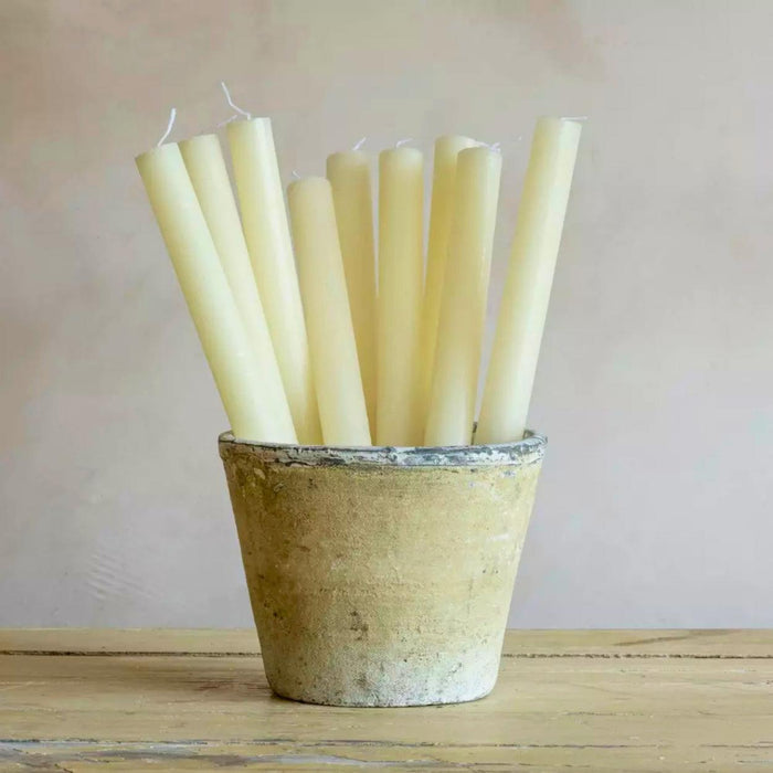 Set of six unlit candles in a rustic pot on a wooden surface with a neutral background